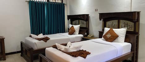 A hotel room with two beds, a window with curtains, a wall-mounted air conditioner, and a telephone on the nightstand.