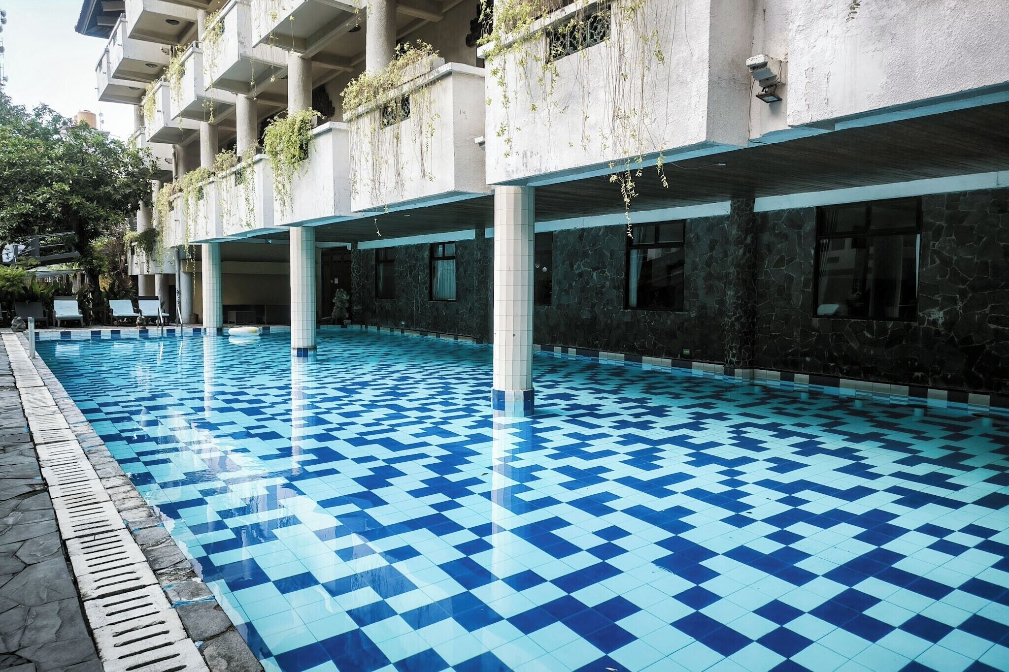 A swimming pool with a checkered floor pattern, surrounded by a building with columns and balconies.
