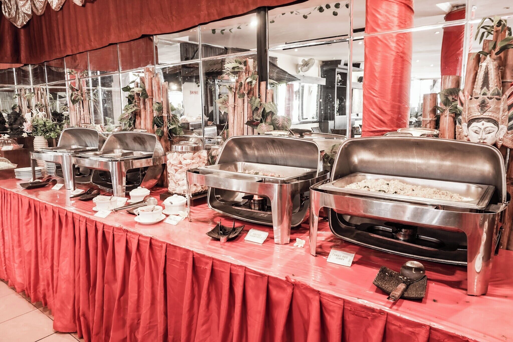 A buffet setup with multiple food stations, including a section for fried rice and curry, and a variety of dishes displayed on stainless steel serving trays.