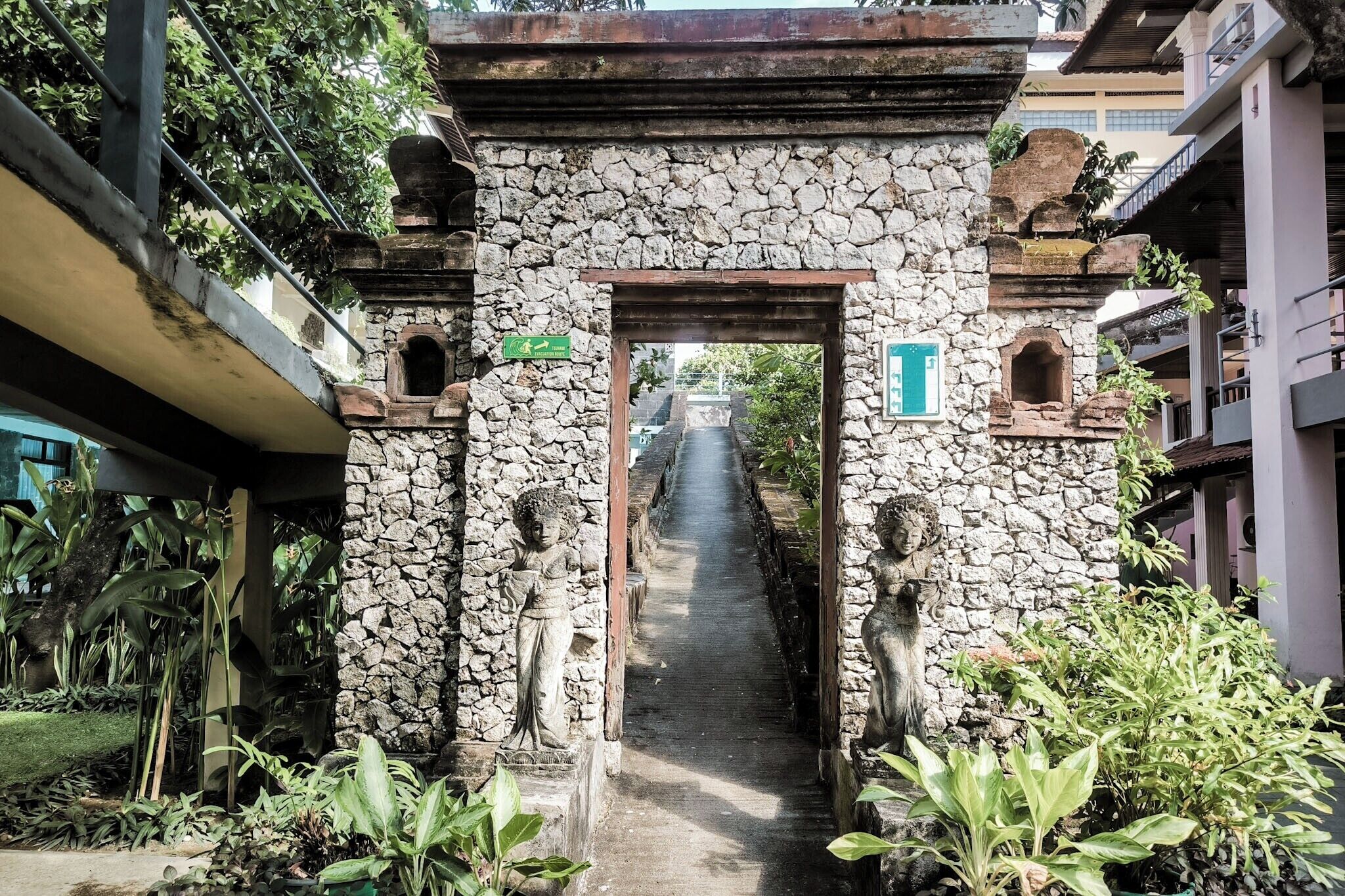 A stone archway leading to a pathway flanked by statues and lush greenery.