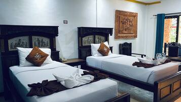 A hotel room with two beds, each with a wooden headboard, white linens, and brown decorative pillows. There is a wall-mounted telephone and a framed artwork above the beds.