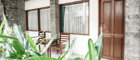 A room with a wooden door, a window with curtains, a table with chairs, and large green plants.