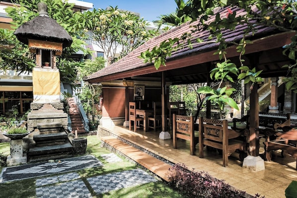 A traditional wooden structure with a thatched roof, surrounded by lush greenery and stone steps leading to a covered seating area. - Melasti Kuta Beach Hotel and Spa (Kuta)