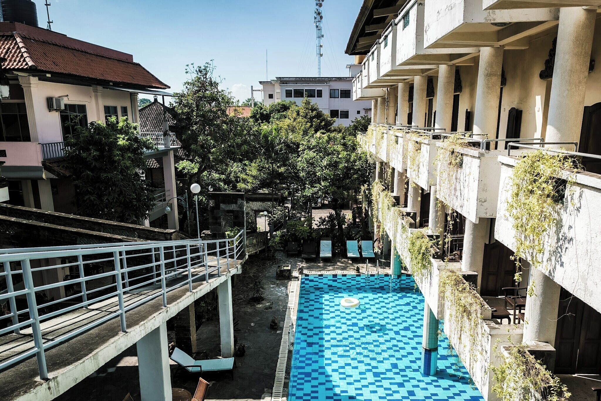 A swimming pool with a checkered pattern, surrounded by buildings with balconies and vegetation.