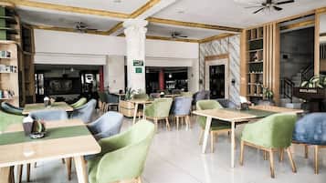 A restaurant with multiple tables and chairs, a ceiling fan, marble walls, and a sign indicating a meeting room.