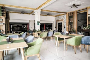 Un restaurante con varias mesas y sillas, un ventilador de techo, paredes de mármol y un letrero que indica una sala de reuniones.