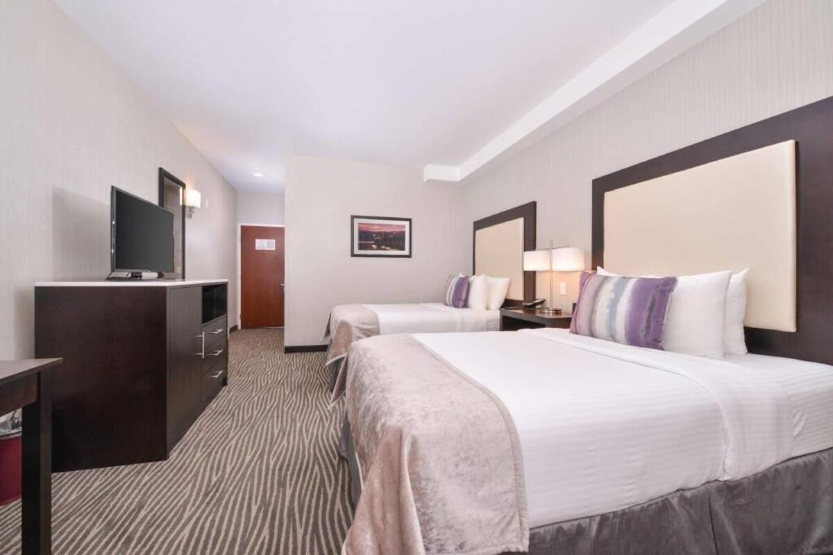 A hotel room with two beds, a TV, a desk, and a door.