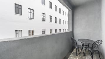 Un balcón con un edificio blanco al fondo, dos sillas de metal y una mesa redonda pequeña.