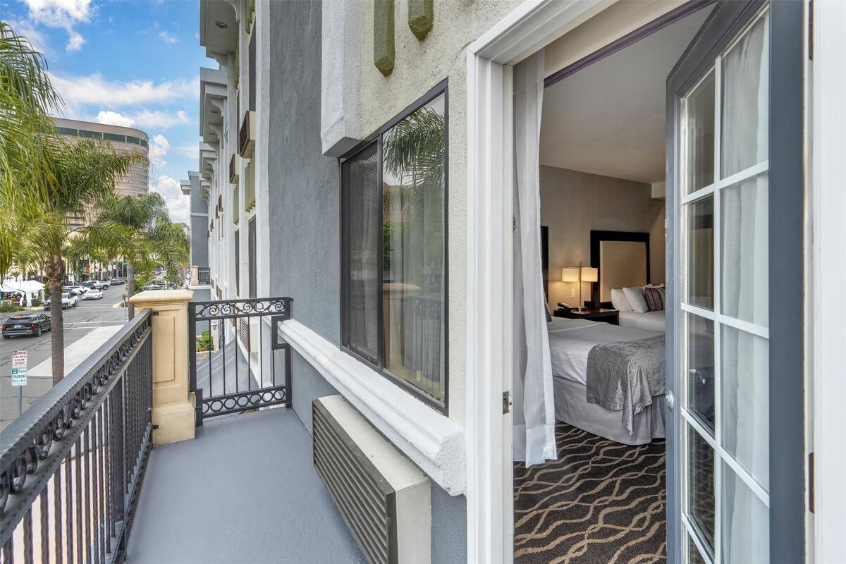 A hotel room with a balcony, a bed with a headboard, and a view of the street.