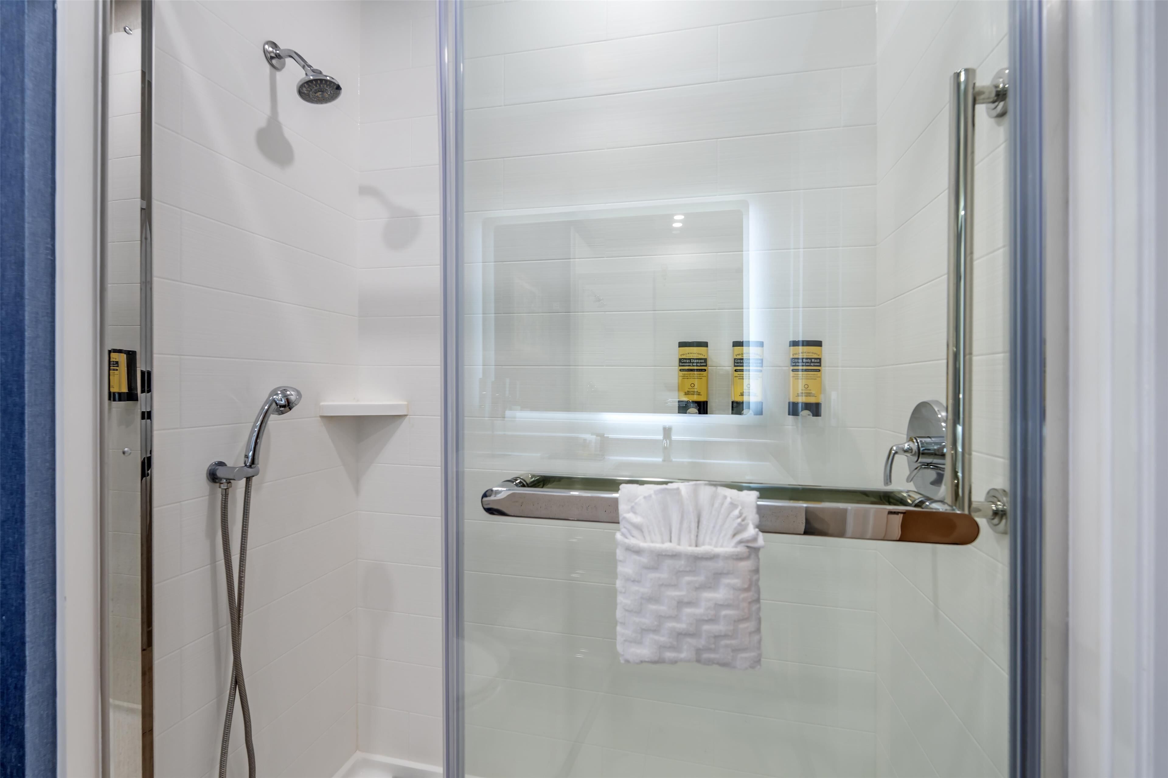 Un espace douche fermé par des parois de verre, doté d’un pommeau de douche à main, d’une porte en verre et d’un porte-serviettes avec une serviette pliée.