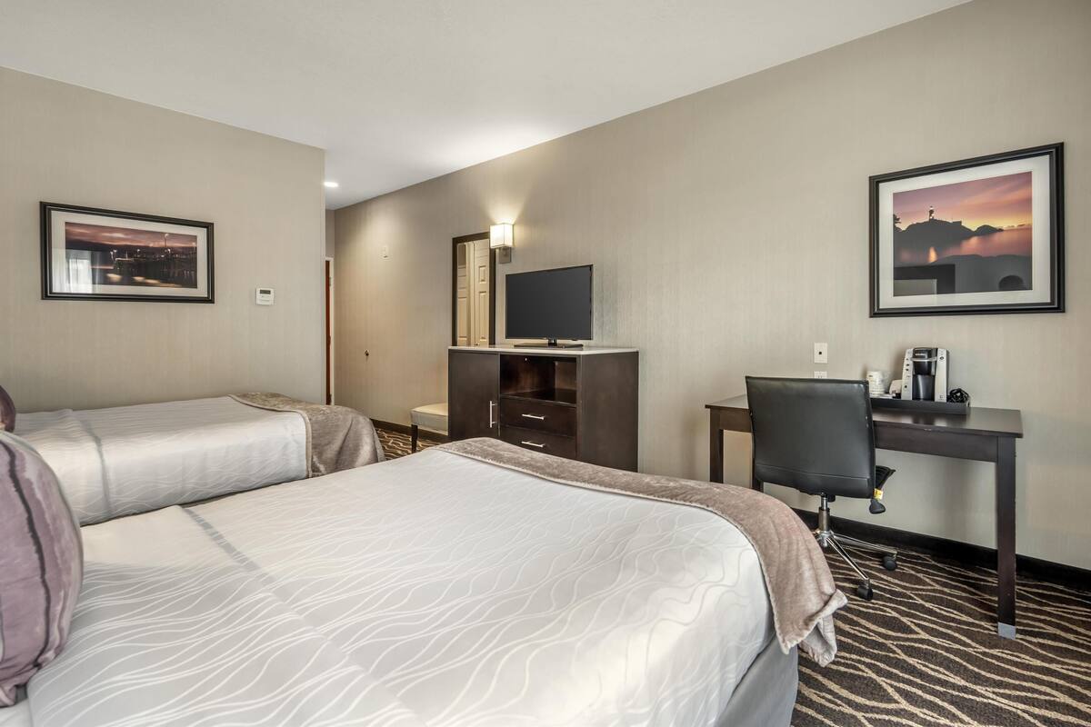 A hotel room with two beds, a desk, a chair, a TV, and two framed pictures on the walls.