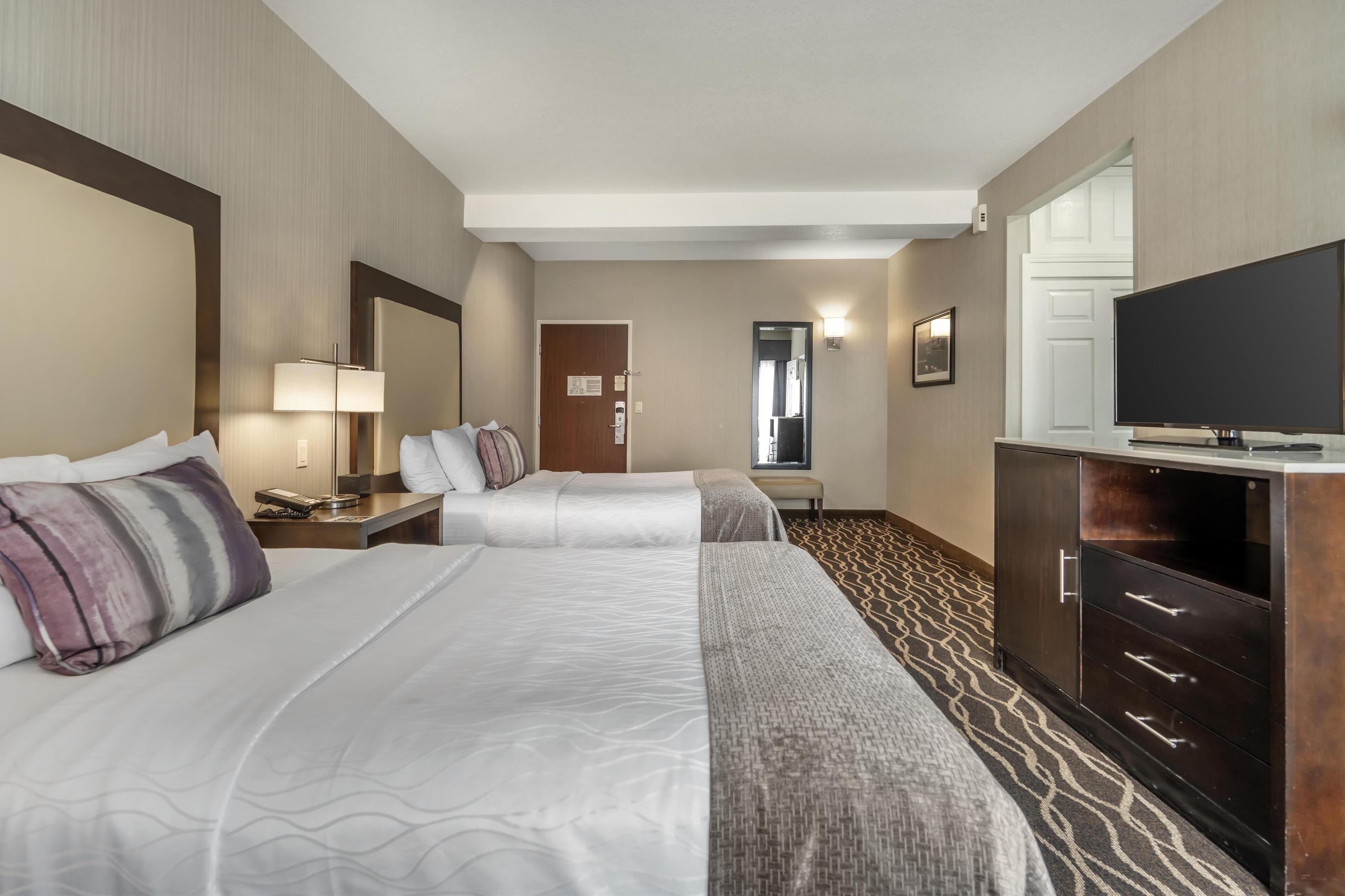 A hotel room with two beds, a TV, a desk with a lamp, and a wardrobe.