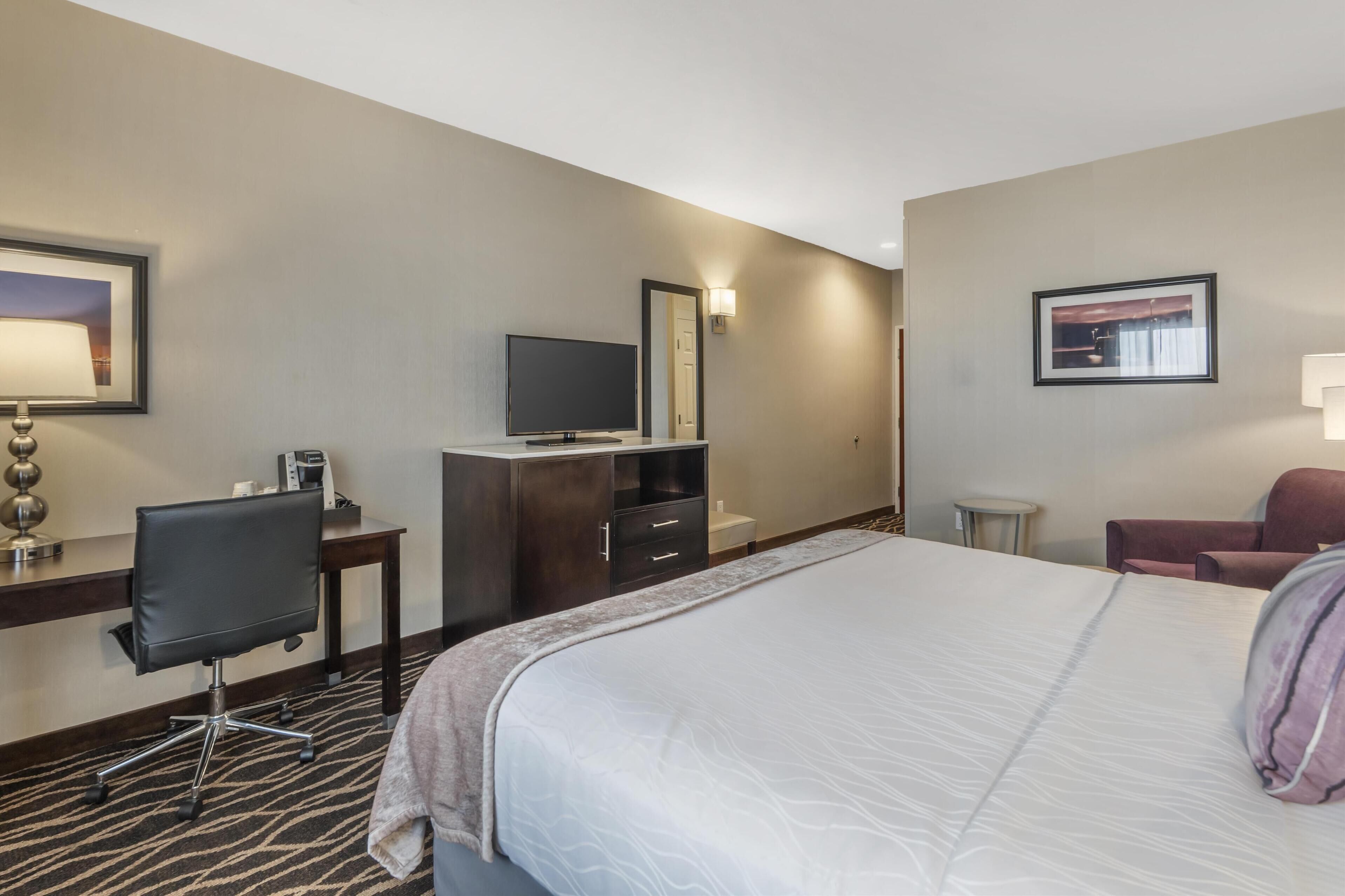 Een hotelkamer met een groot bed, een bureau met een computer, een televisie en een stoel.