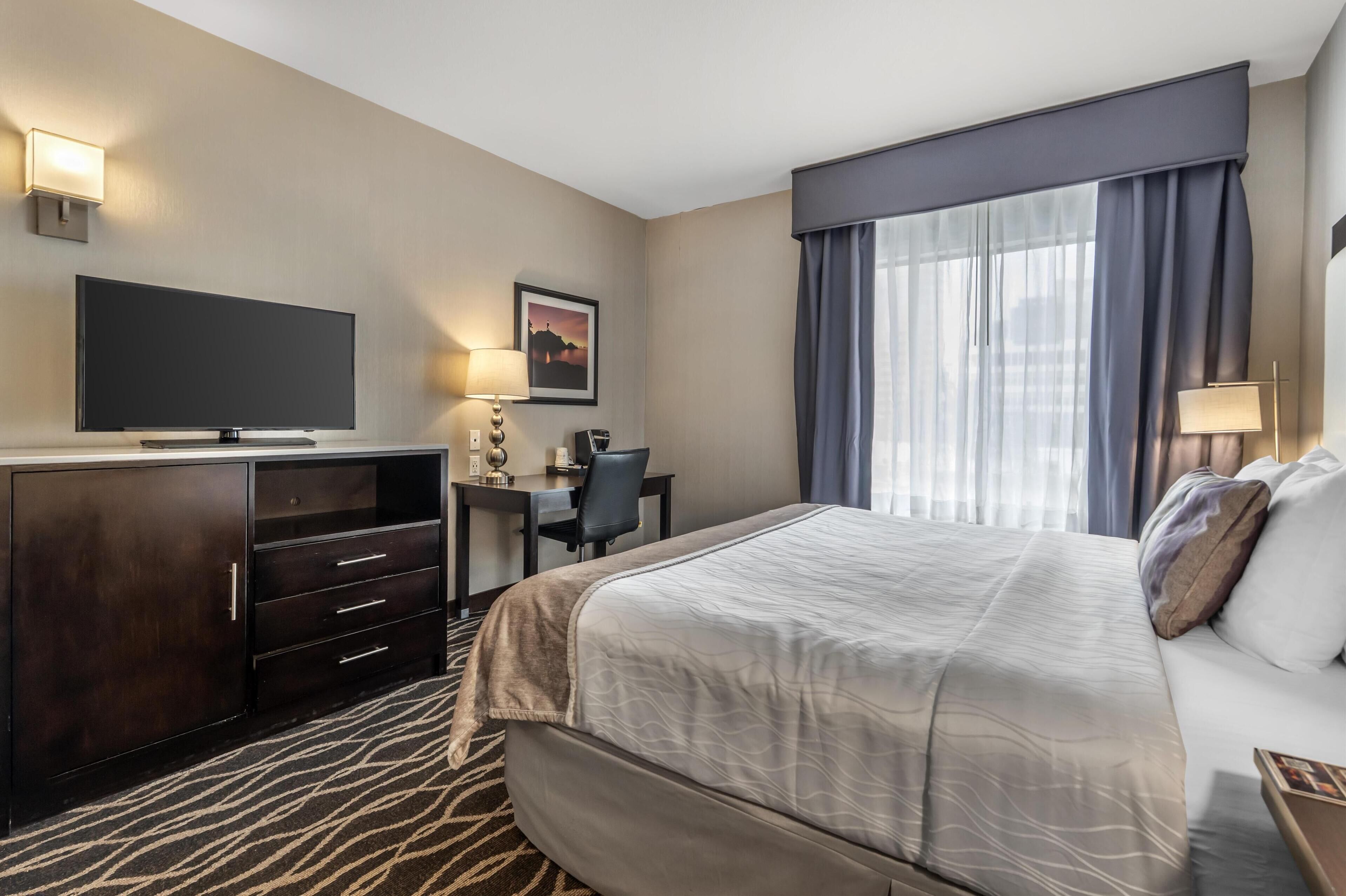 A hotel room with a large bed, a desk with a chair, a television, and a window with curtains.