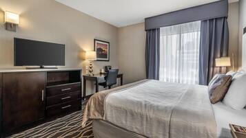 A hotel room with a large bed, a desk with a chair, a television, and a window with curtains.
