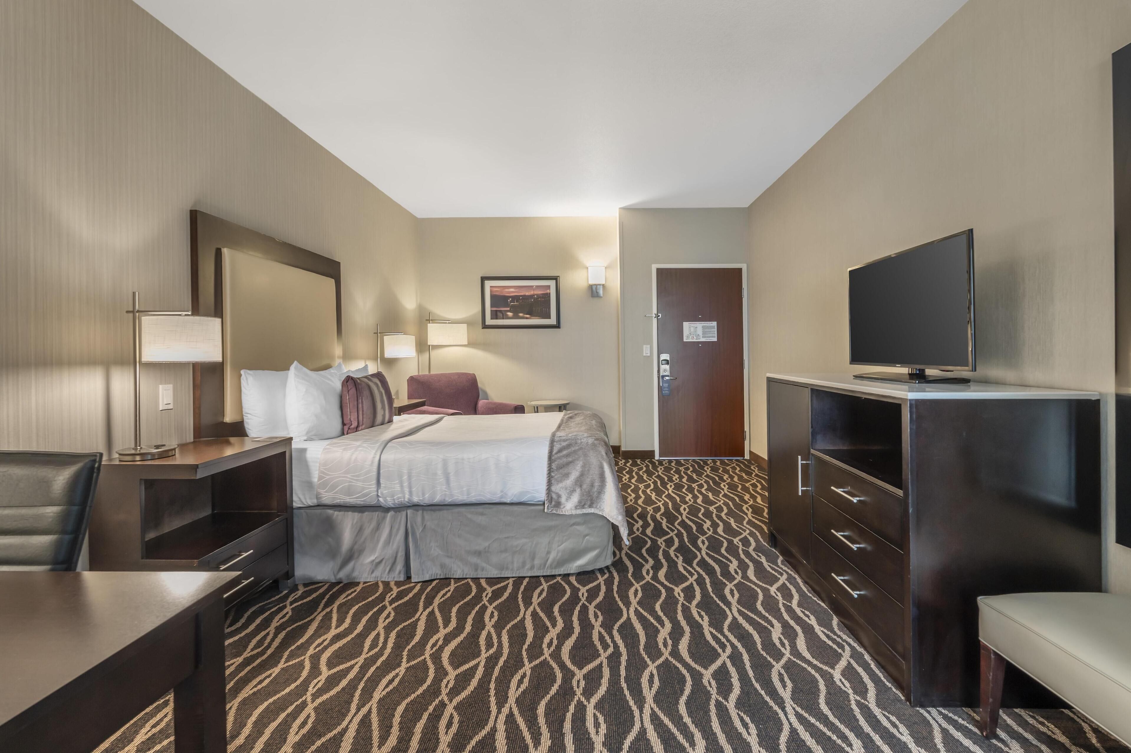Ein Hotelzimmer mit einem Bett, einem Schreibtisch, einem Stuhl, einem Fernseher und einem Kleiderschrank.