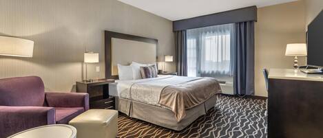 A hotel room with a bed, a desk, a chair, a small table, and a large window with curtains.
