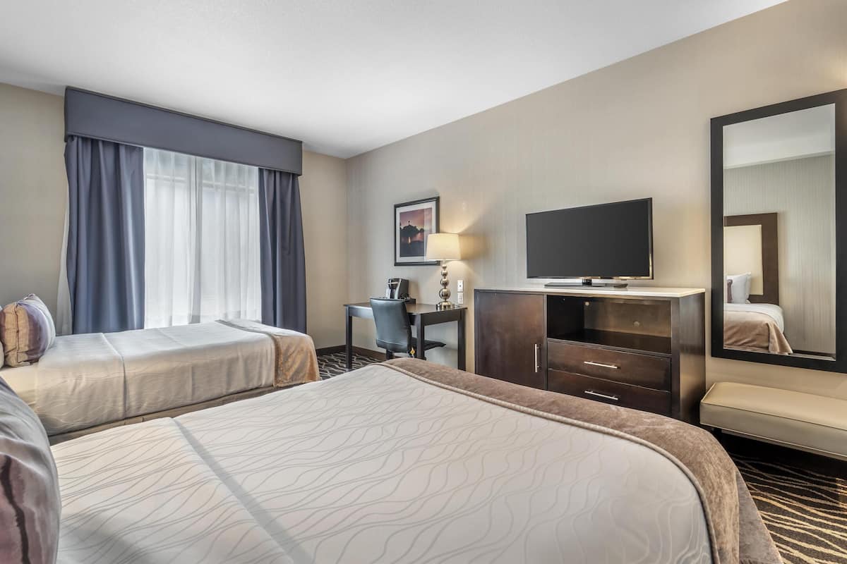 A hotel room with two beds, a desk, a television, and a mirror.