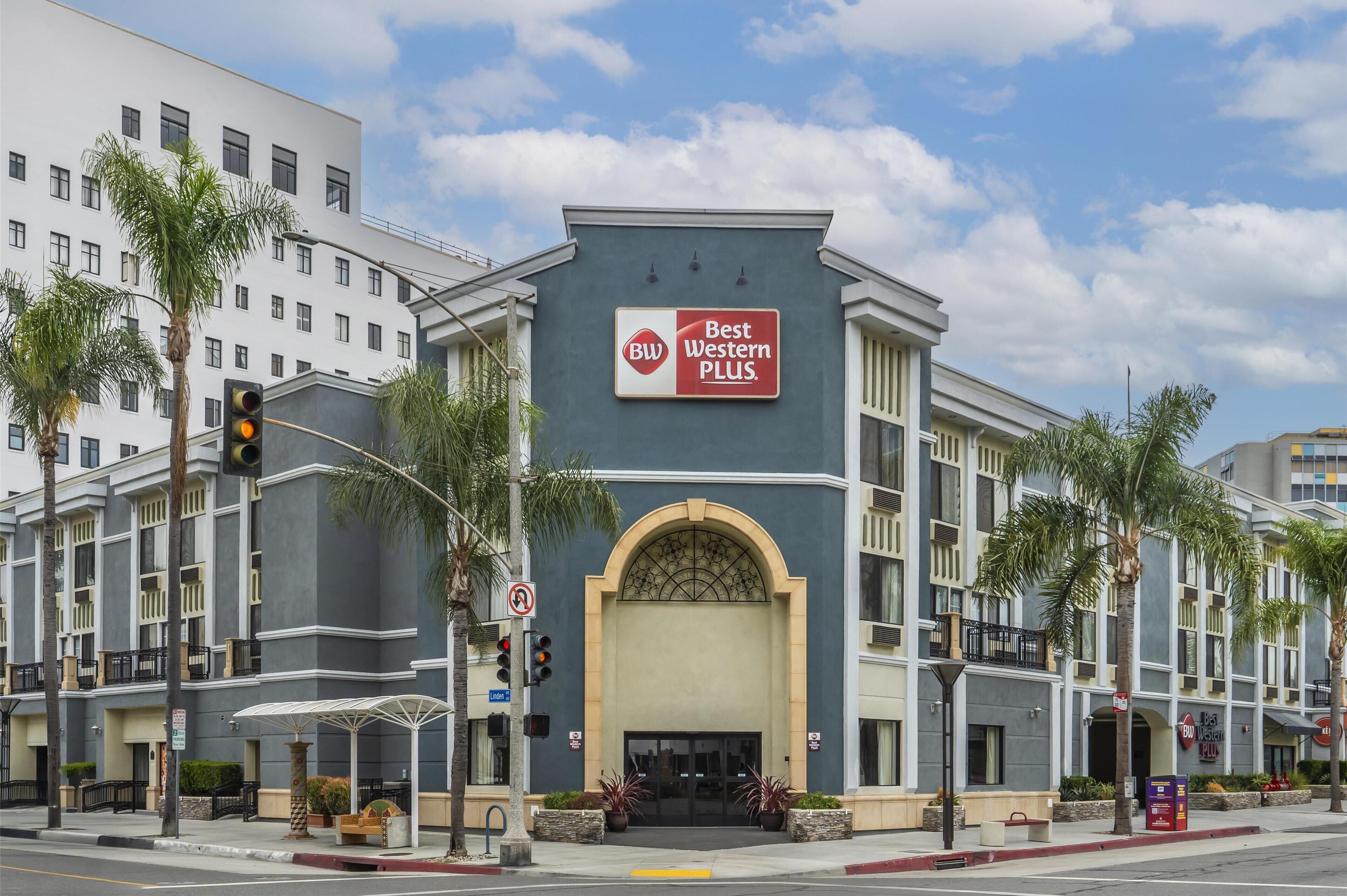 A hotel with a 'Best Western Plus' sign, a large arched entrance, and a modern facade with palm trees and a clear sky.