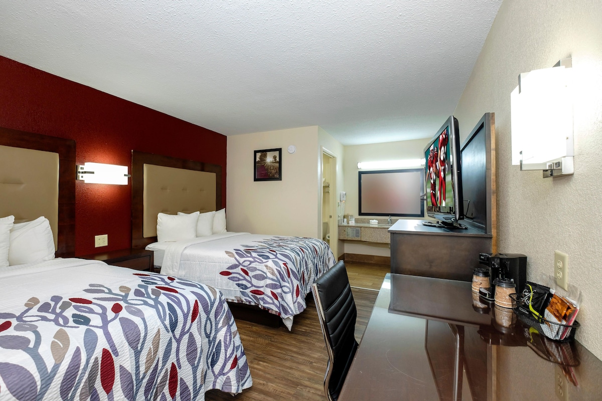 A hotel room with two beds, a desk, a television, and a coffee maker.