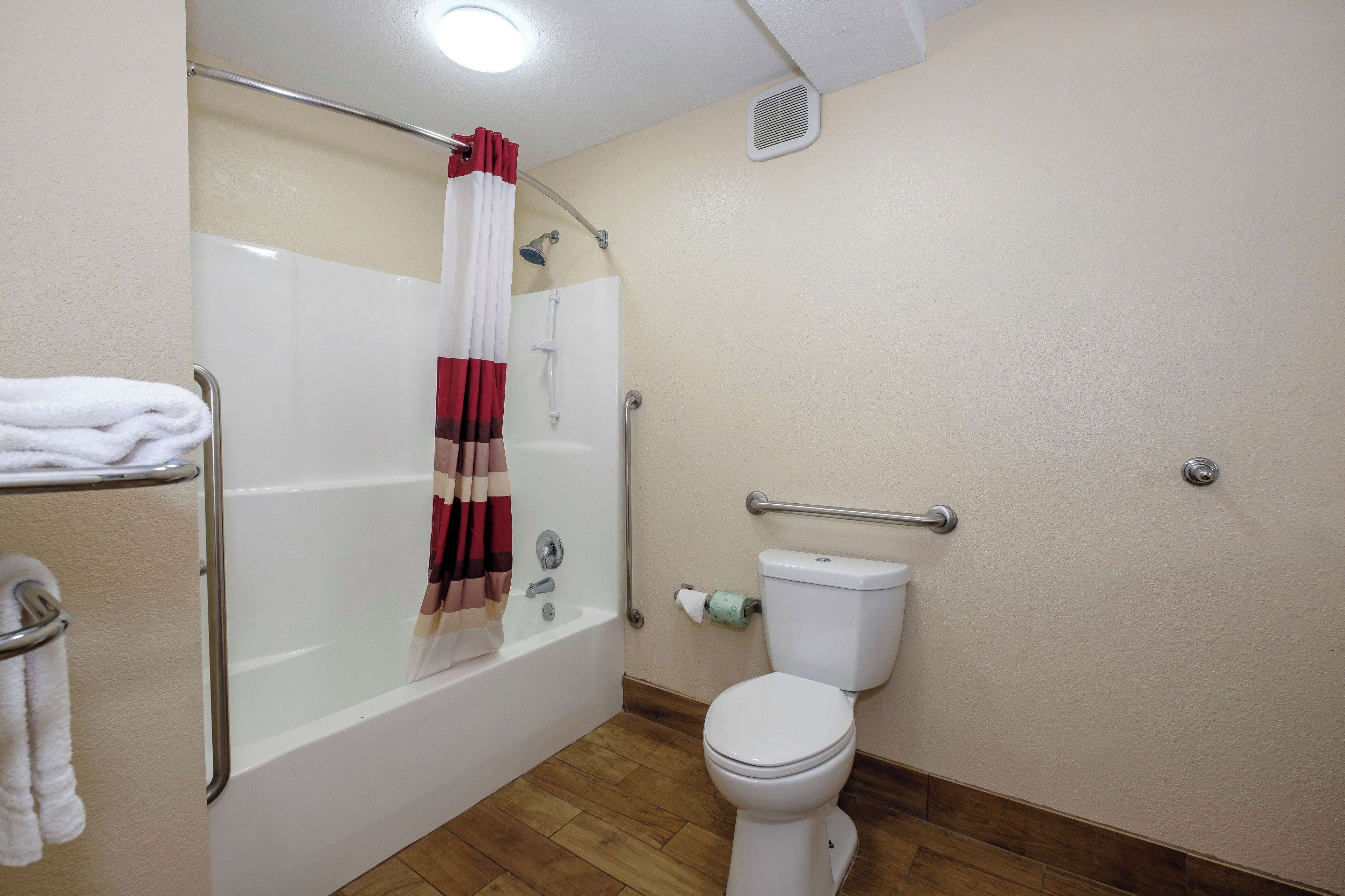 Un baño con bañera, inodoro y barras de apoyo.