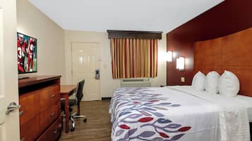 A hotel room with a bed, a desk, a chair, a dresser, a door, and a window with curtains.