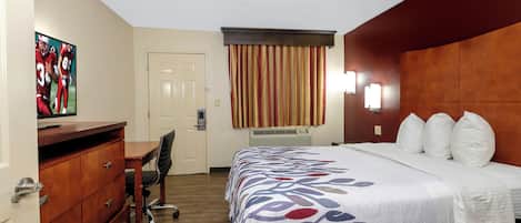 Habitación de hotel con cama, escritorio, silla, cómoda, puerta y ventana con cortinas.