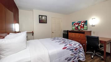 A hotel room with a bed, a desk, a chair, a dresser, a television, and a picture on the wall.