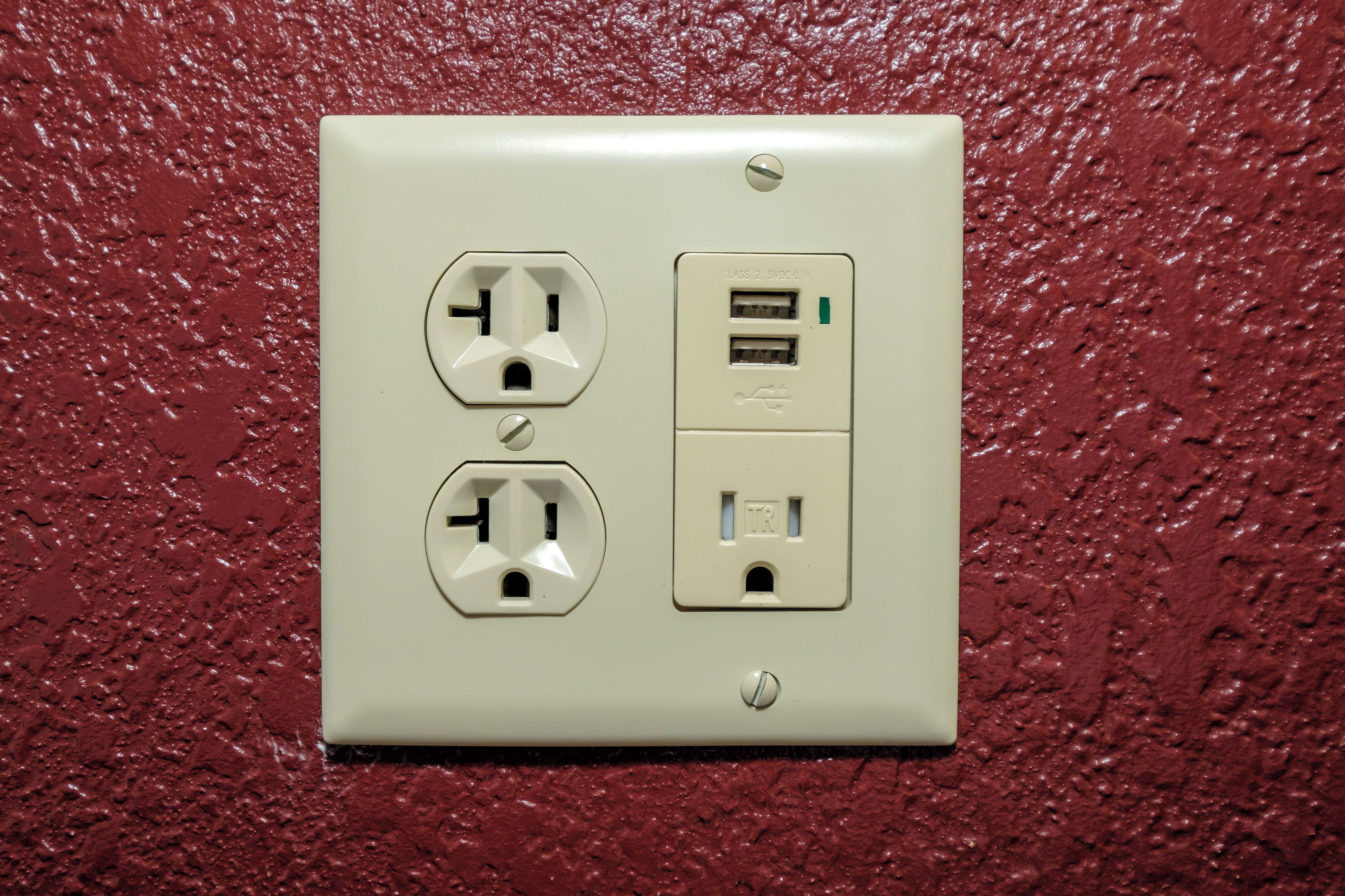 A wall-mounted electrical outlet with two sockets and a USB port, set against a textured red wall.