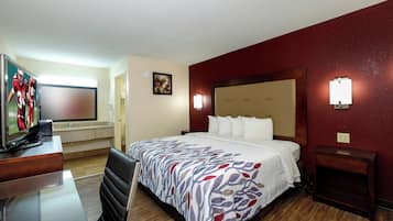 Ein Hotelzimmer mit einem Bett, einem Schreibtisch mit Fernseher, einem Sessel und einem Nachttisch.