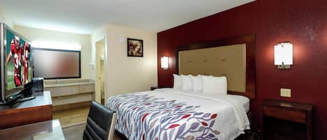 A hotel room with a bed, a desk with a television, a chair, and a nightstand.