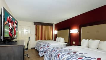 Quarto de hotel com televisão, cama, escrivaninha e janela com cortinas.