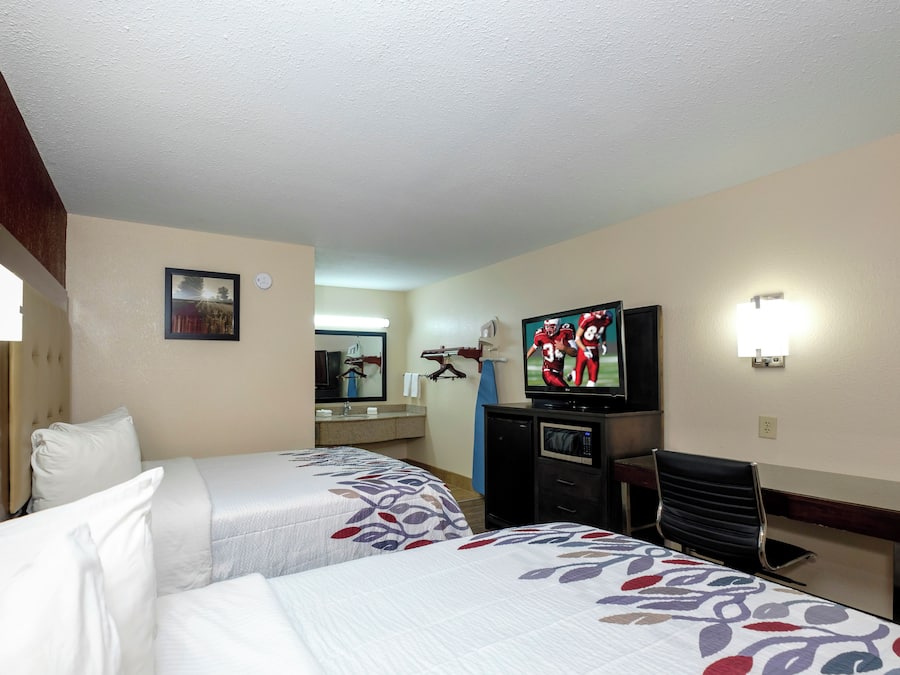 A hotel room with two beds, a television, a desk, and a mirror.