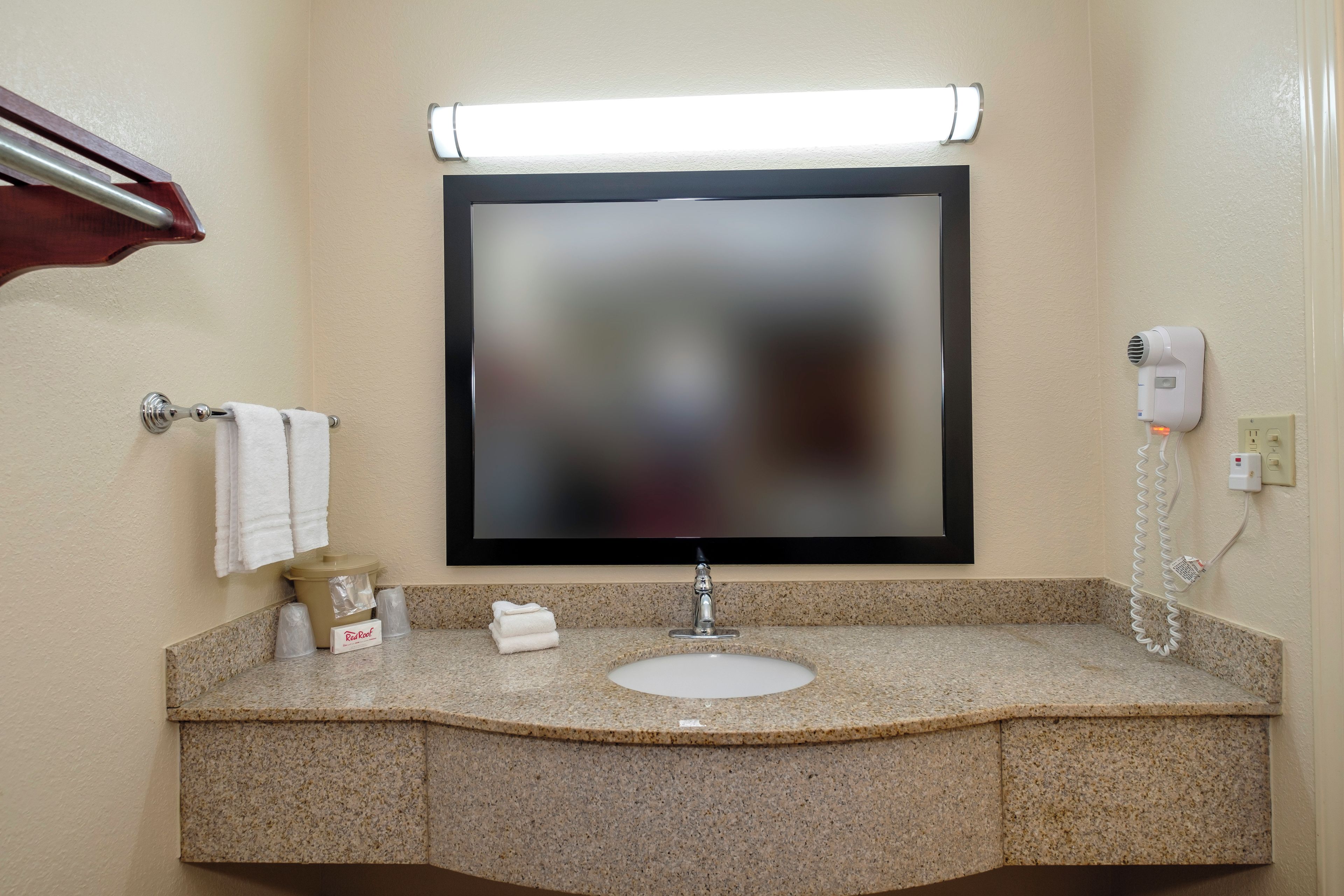 A bathroom with a granite countertop, a sink, a mirror, a towel rack, and a hairdryer.