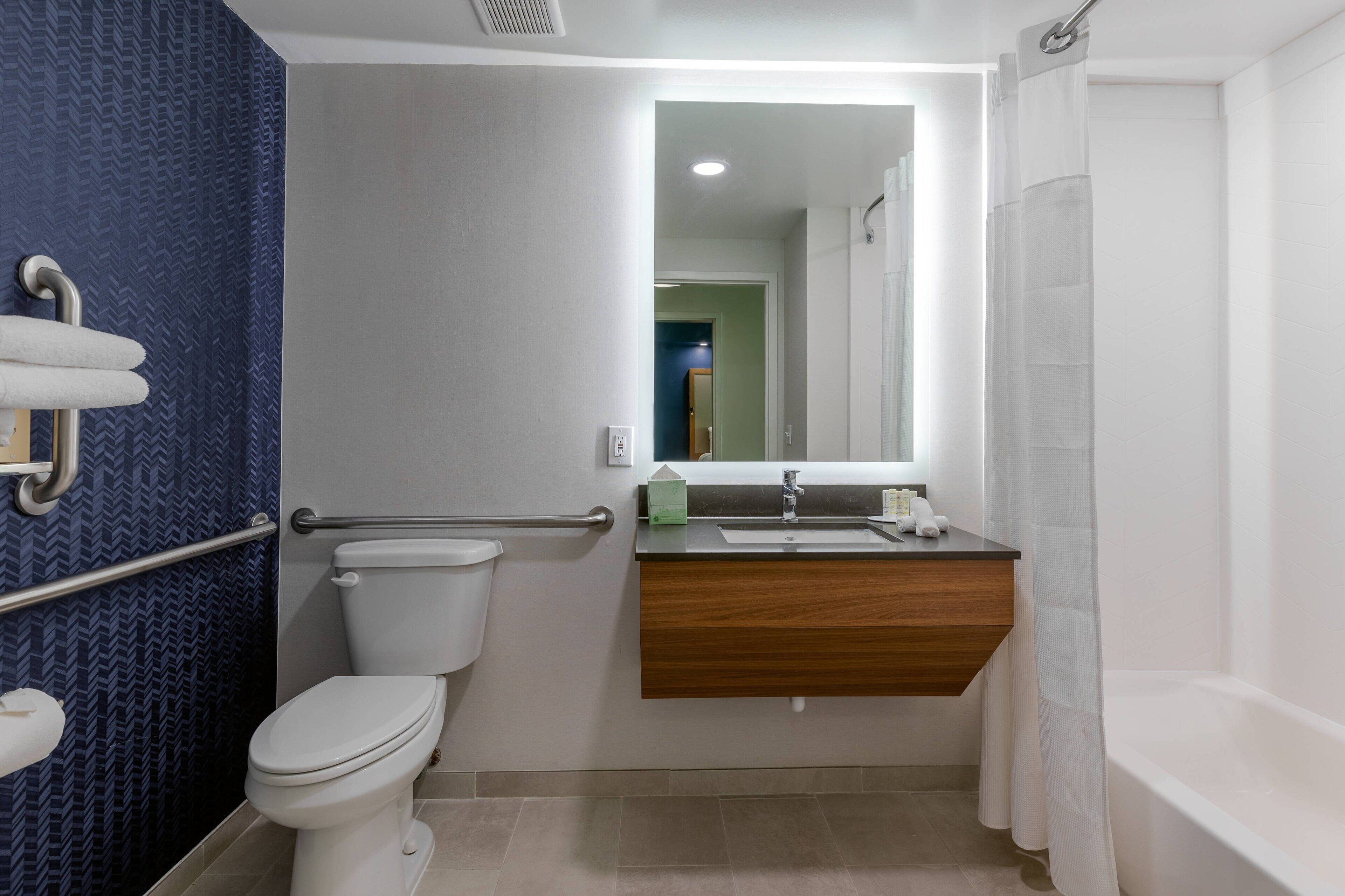 A bathroom with a white toilet, a wooden vanity with a mirror, a bathtub, and a blue patterned wall.