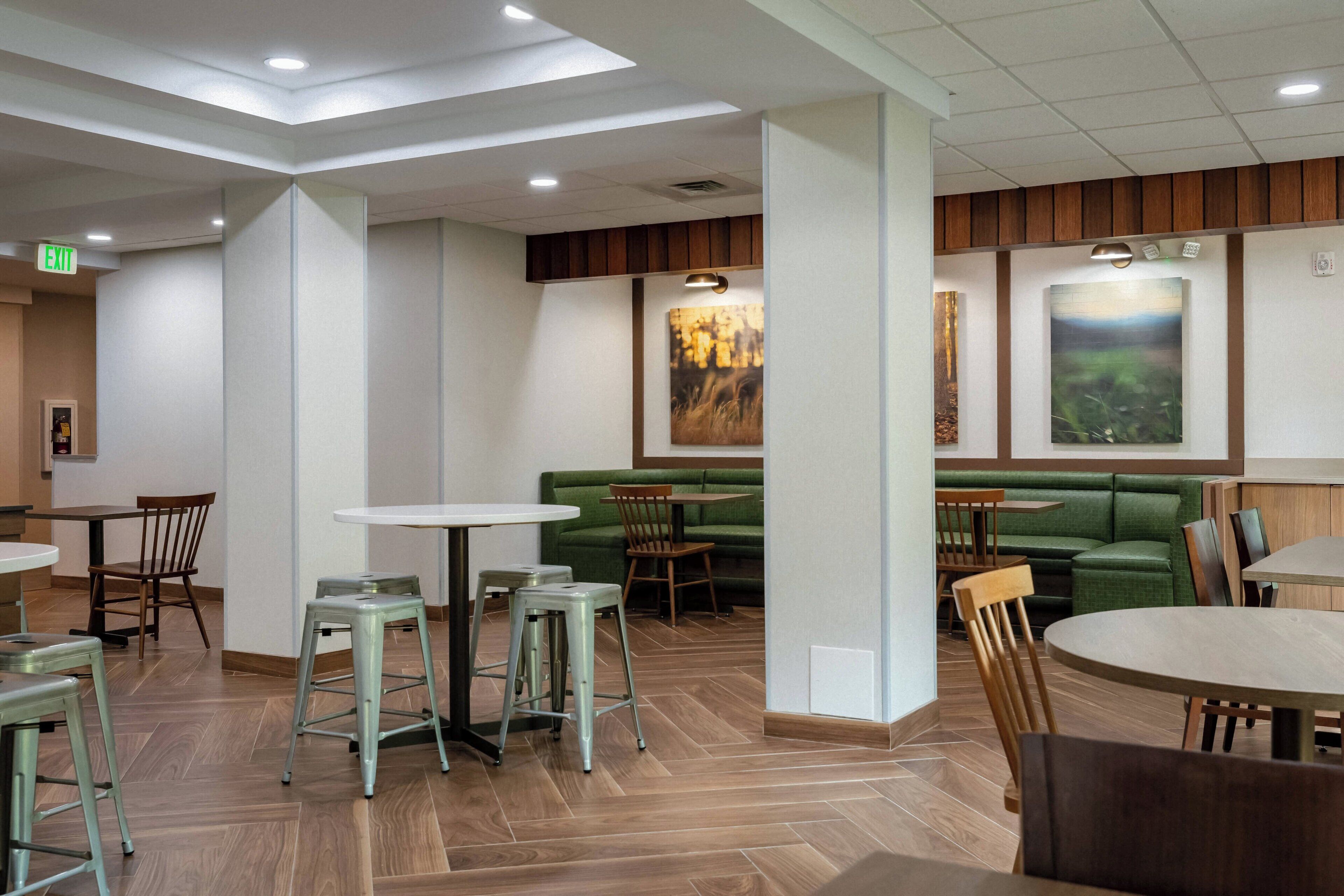 A modern restaurant with high ceilings, recessed lighting, and a mix of seating options including tables and a green booth area.