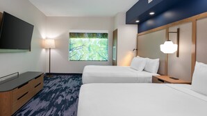 Une chambre d’hôtel avec deux lits, une télévision, une lampe et une grande fenêtre donnant sur la forêt.