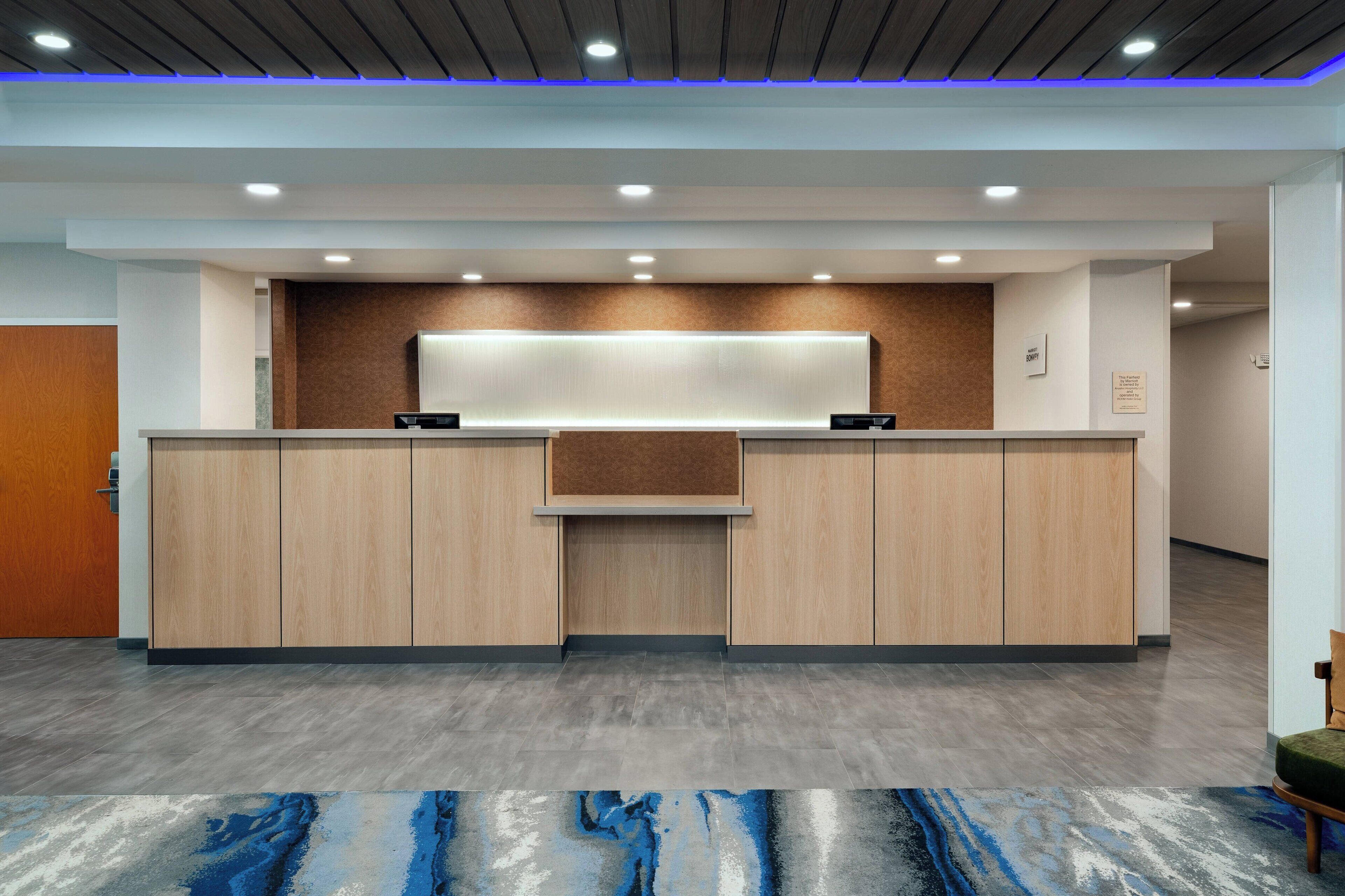 Un área de recepción con un mostrador de madera, un panel informativo en la pared y piso gris.