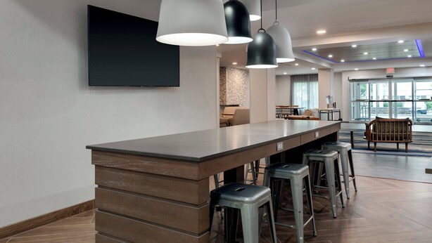 Une cuisine moderne dotée d’un long comptoir, de tabourets de bar, de luminaires suspendus et d’un téléviseur à écran plat fixé au mur.