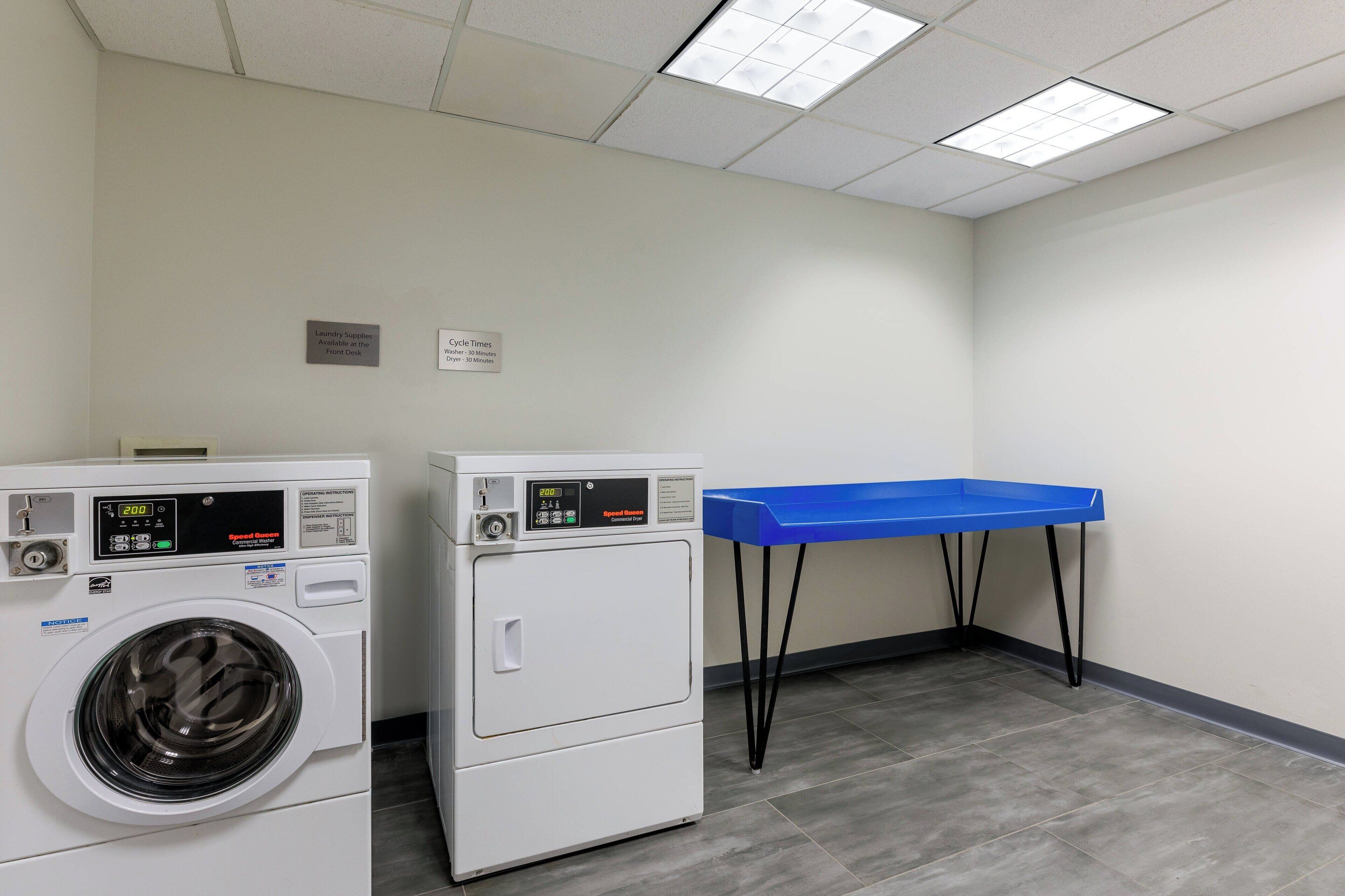 A laundry room with two front-loading washing machines and a blue drying rack.
