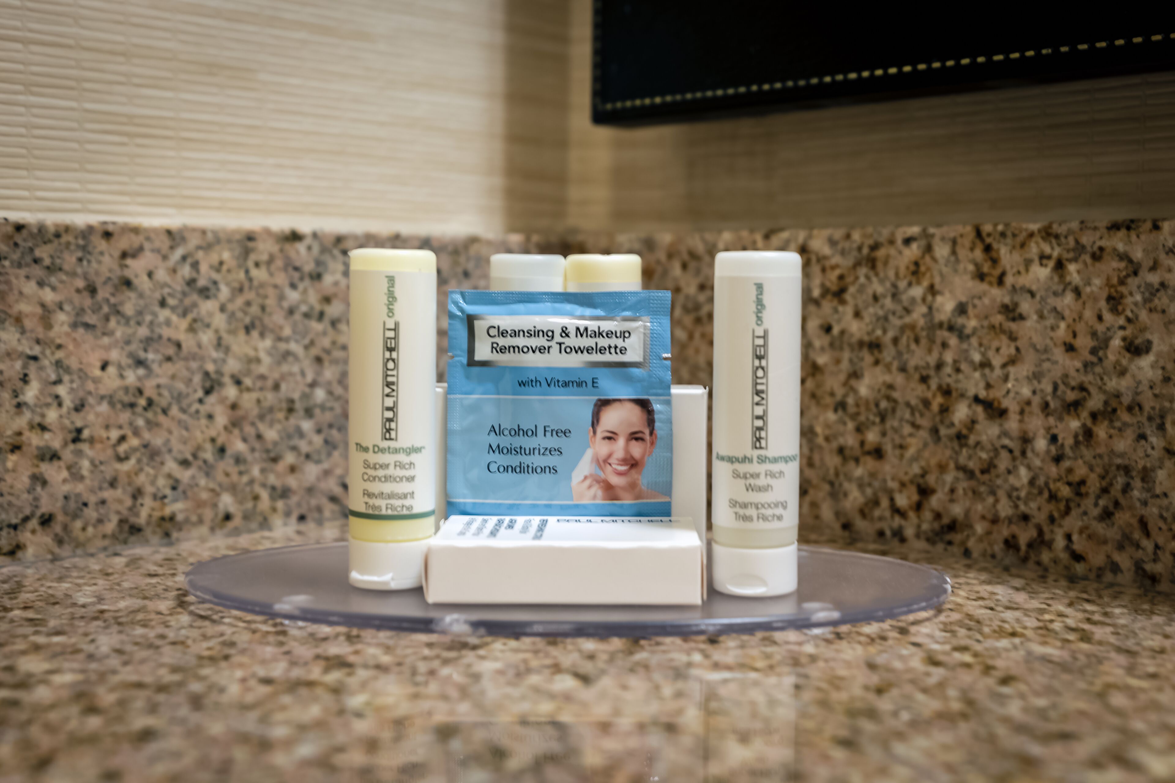 A bathroom counter with a variety of personal care products including a cleansing and makeup remover towelettes, a rich conditioner, and a super rich shampoo.