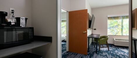 A hotel room with a microwave, refrigerator, and a small table with a chair.