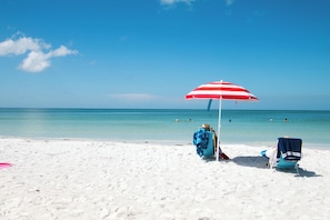 A beach scene with a red and white striped umbrella, two beach chairs, and the ocean in the background. - voco Sarasota by IHG (Sarasota)