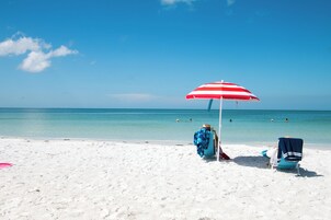 A beach scene with a red and white striped umbrella, two beach chairs, and the ocean in the background.