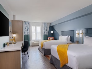 Ein Hotelzimmer mit zwei Betten, einem Schreibtisch, einem Stuhl, einem Fernseher und einem Fenster mit Vorhängen.