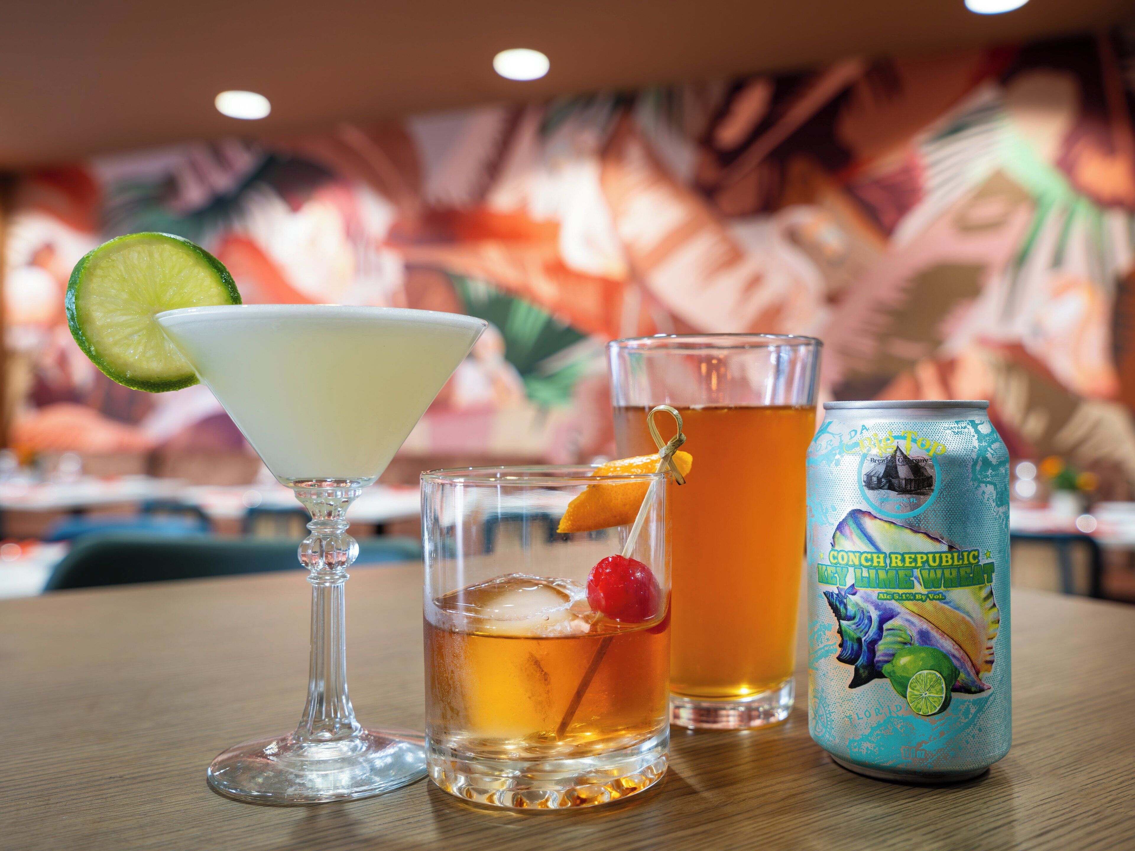 A table with a martini glass, a short glass with a cherry, and a can of beer.