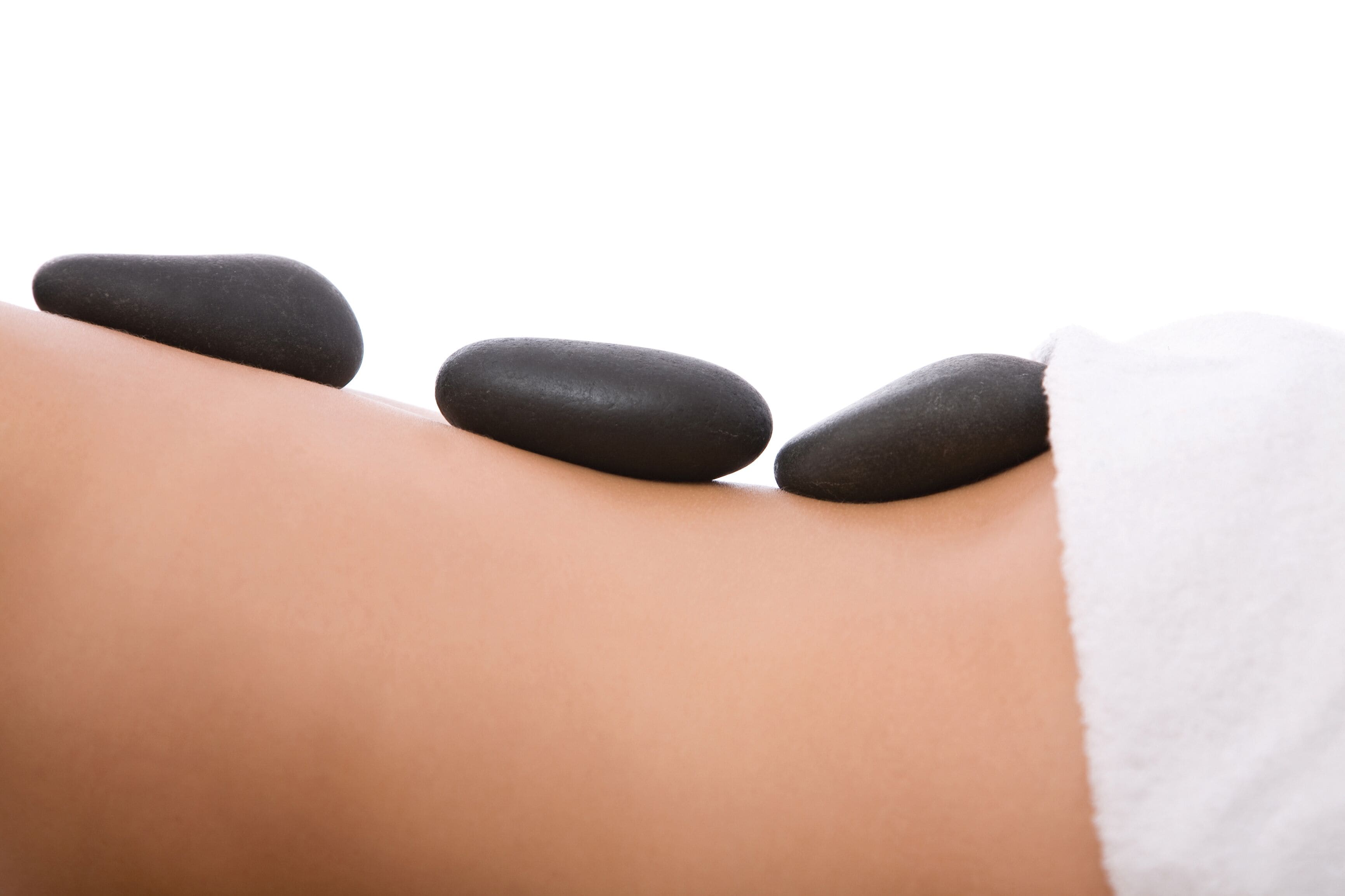 Gros plan d’un massage où l’on voit trois pierres noires posées sur le dos d’une personne.