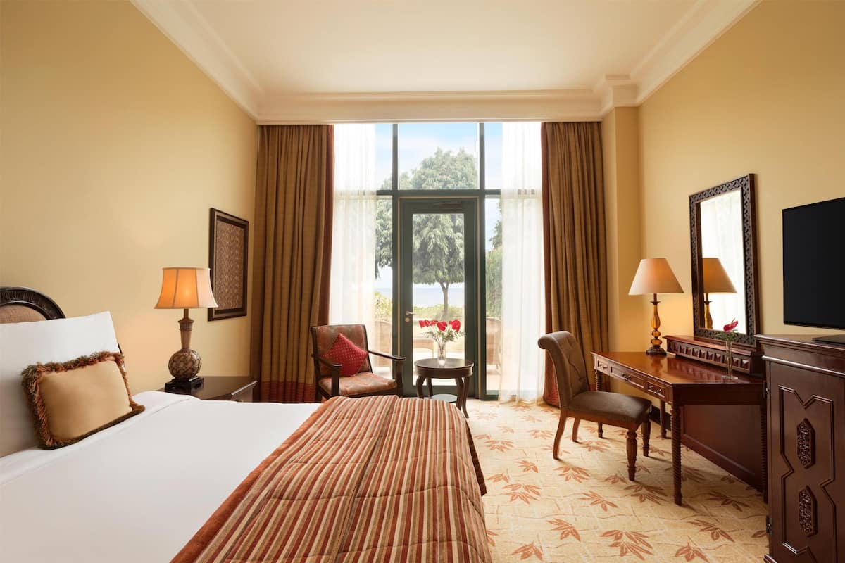 A hotel room with a bed, a desk, a chair, a lamp, a television, and a view of the outdoors.