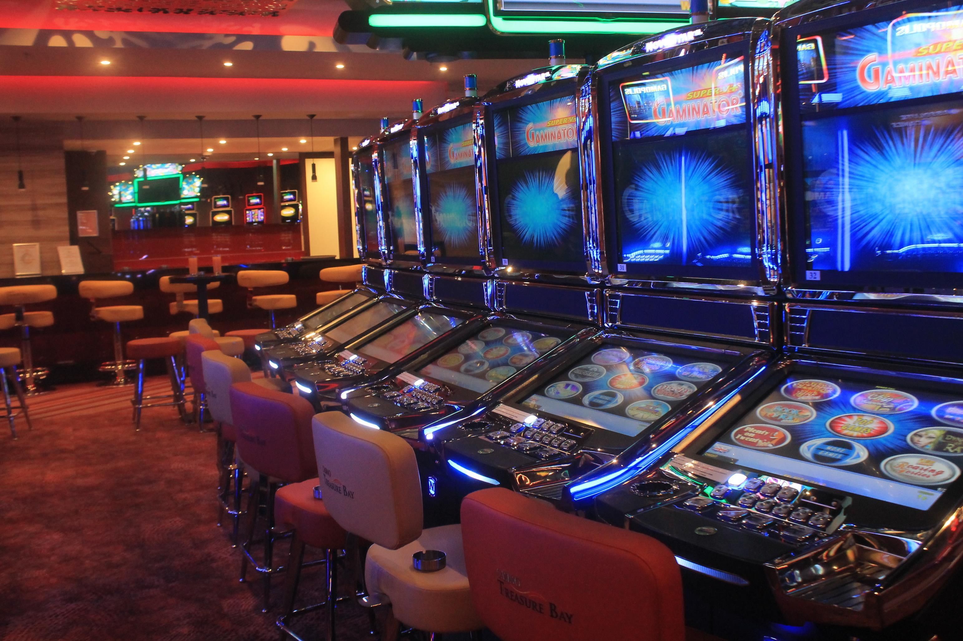 Eine Reihe von Spielautomaten mit beleuchteten Bildschirmen, vor denen Sitzhocker stehen.
