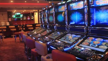 Eine Reihe von Spielautomaten mit beleuchteten Bildschirmen, vor denen Sitzhocker stehen.